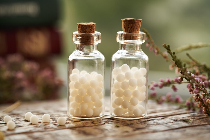 Two bottles of white homeopathic pills or globules with dried herbs and homeopathic books Two bottles of white homeopathic pills or globules with dried herbs and homeopathic books